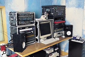 Racks in a rack, including (left rack): a Roland MPG80 Super Jupiter Programmer & MKS80 synth, Waldorf MIDI bay, Roland A110 MIDI display and M480 48‑ input line mixer; (right rack) Studio Electronics SE1 'Minimoog in a rack', Sequential Prophet VS, Clavia Nord Rack, Yamaha TX802, Emu Vintage Keys, Novation DrumStation & BassStation rack, Akai S3000 sampler. The Novation BassStation keyboard is also visible on the right.