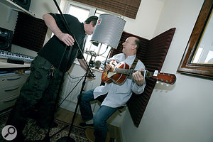 Paul tries out mics and placements for recording John's guitar and vocals. The foamed corner and Reflexion Filter dried up the room ambience on John's recordings — but perhaps a little too much?